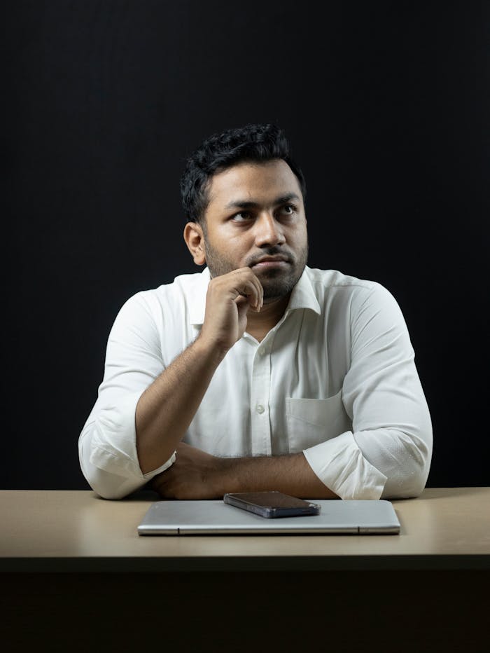 Thoughtful businessman seated at a desk with a laptop and phone, deep in reflection.