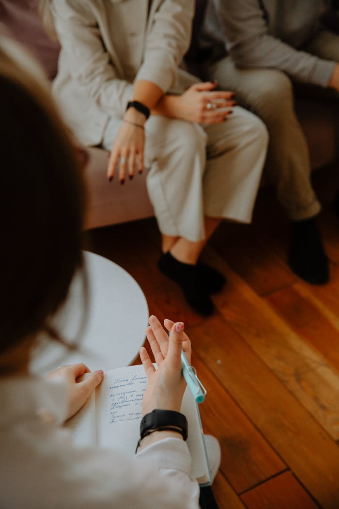 A therapy session with a counselor taking notes while clients discuss issues on a couch.